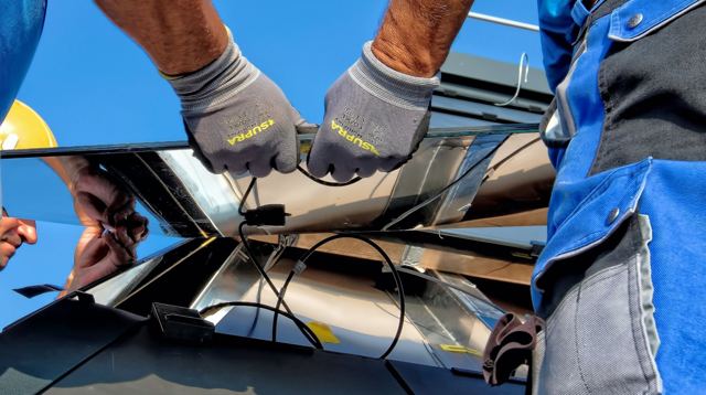Solar installer wearing gloves working on wiring under a solar panel