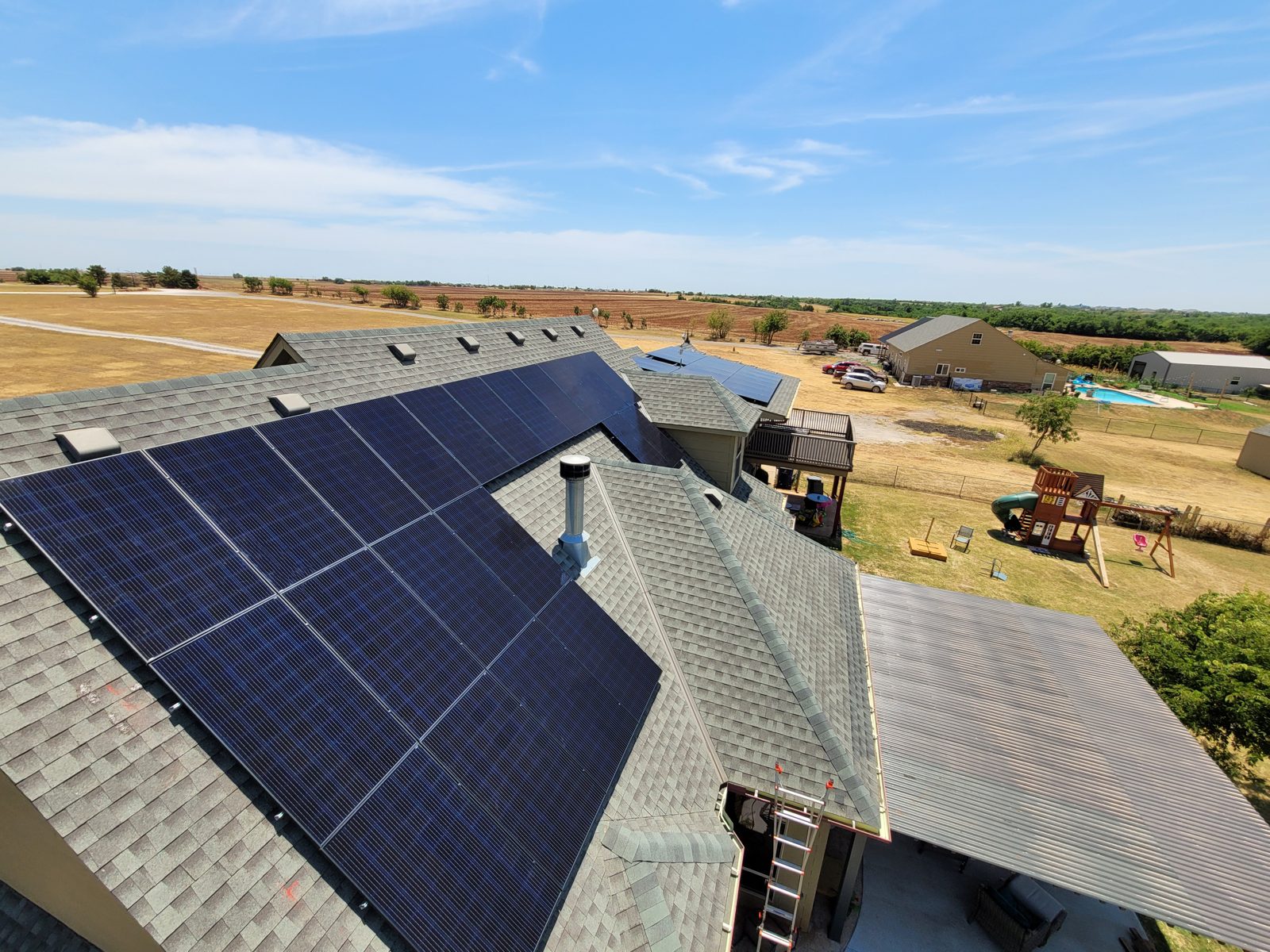 Solar panels installed on a shingle roof with open Oklahoma farmland in the background